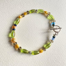 Beaded bracelet with green, yellow, and clear beads and yellow freshwater pearls with just a stop of blue beads on a white background